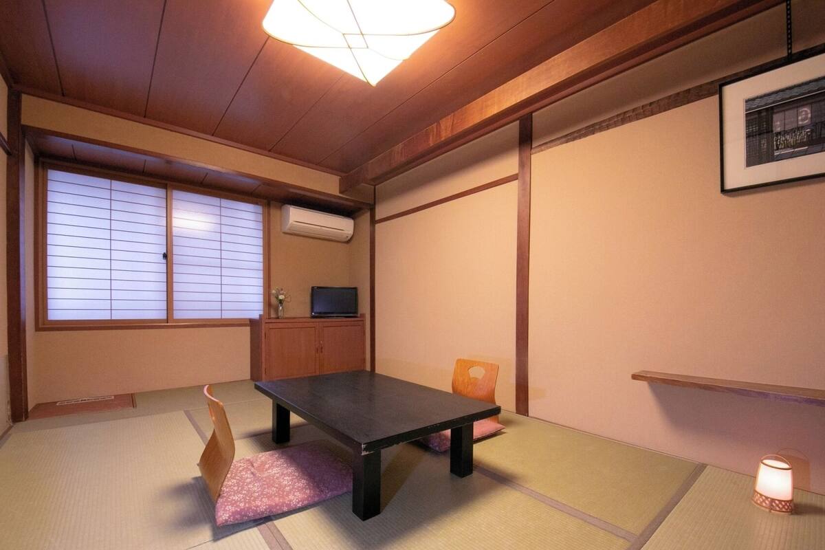 Una habitación tradicional japonesa con suelo de tatami, una mesa baja, un televisor y puertas correderas.