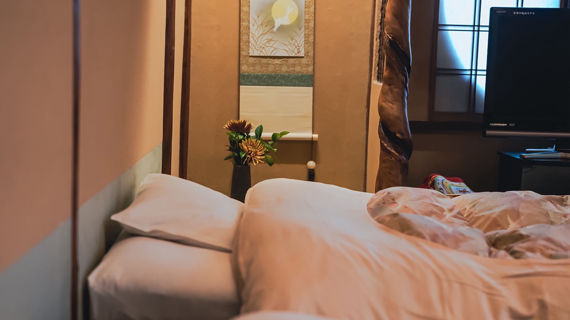 A hotel room with a bed, a vase with flowers, a window with curtains, and a television.