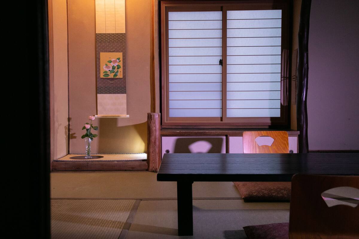 Una habitación japonesa tradicional con suelo de tatami, ventana con pantalla corredera shoji y una mesa de madera baja.