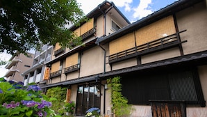 A traditional Japanese building with a wooden exterior, a tiled entrance, and a small garden with purple flowers. - Hokkaikan Ohanabo (Kyoto)