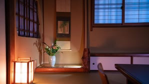 A traditional Japanese room with tatami flooring, a low table, a cushioned bench, a lit lantern, and a framed picture of palm trees. - Hokkaikan Ohanabo (Kyoto)