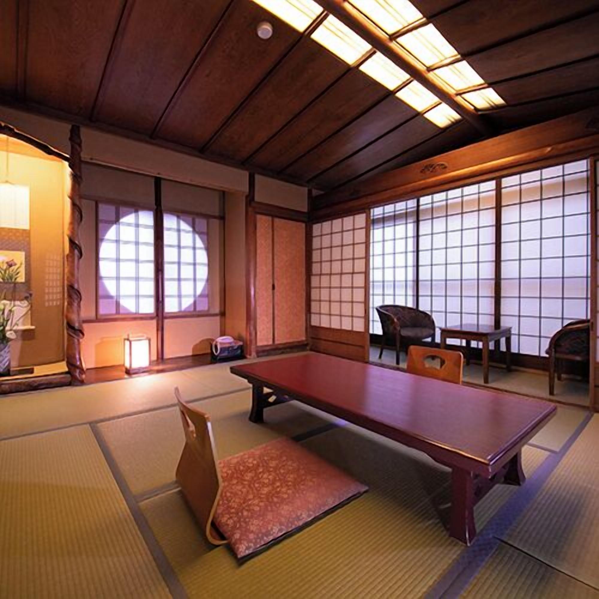 A tatami mat room with a low table and chairs, a sliding door, and a view through a shoji screen.