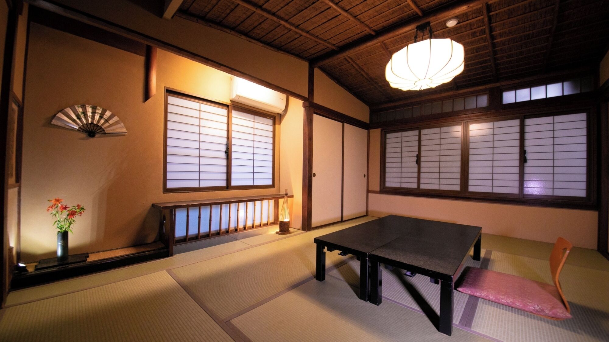 A traditional Japanese room with tatami flooring, a low table, a bench, a fan, and shoji screens.
