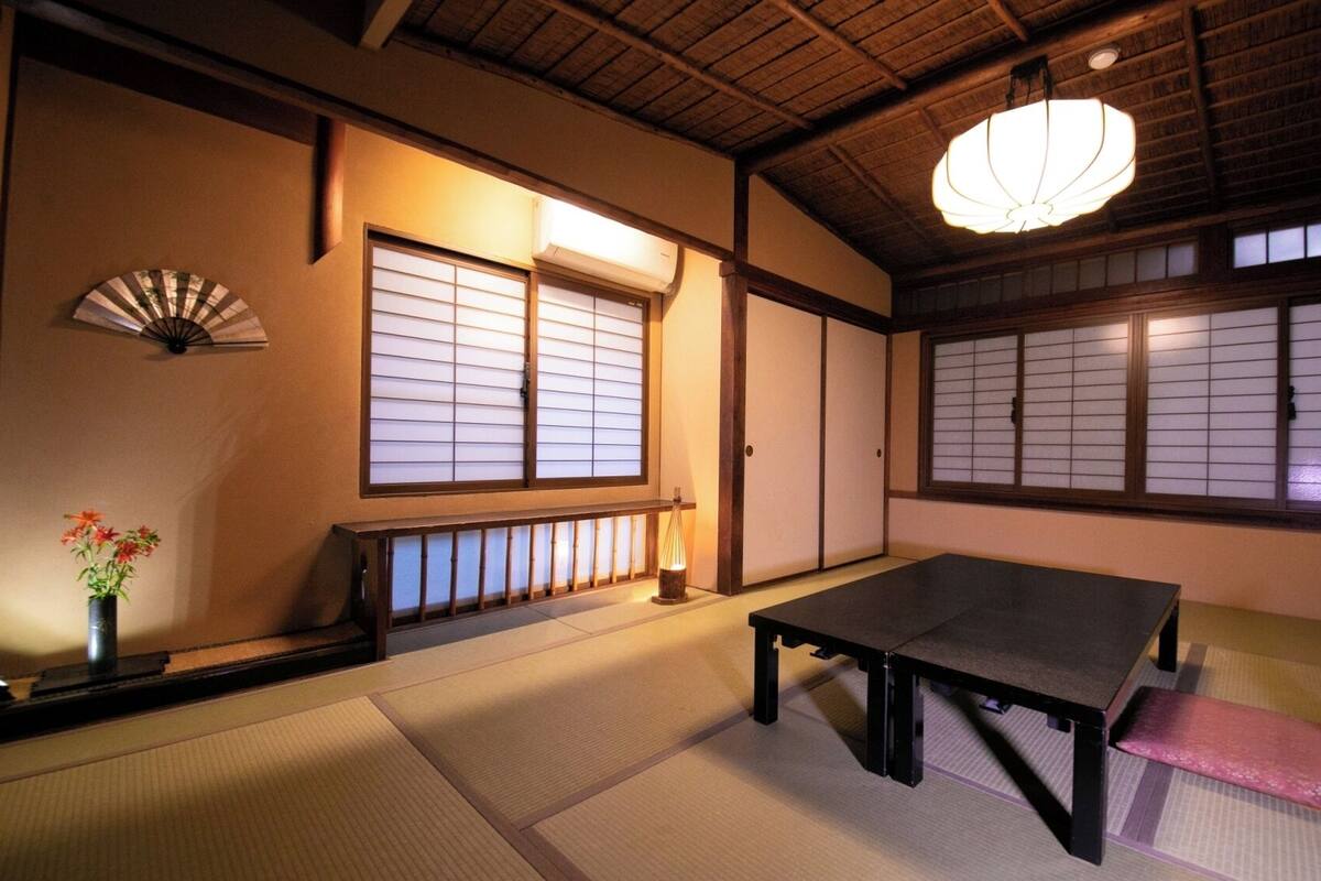 Una habitación japonesa tradicional con suelo de tatami, una mesa baja, un banco, un abanico y puertas shoji.