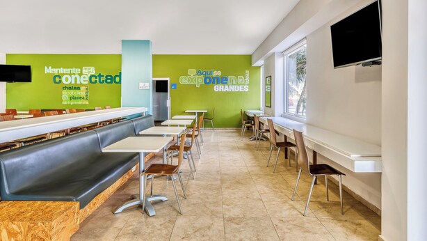 A modern dining area with long communal tables, individual booths, and a flat-screen TV mounted on the wall. - One Salina Cruz (Salina Cruz)