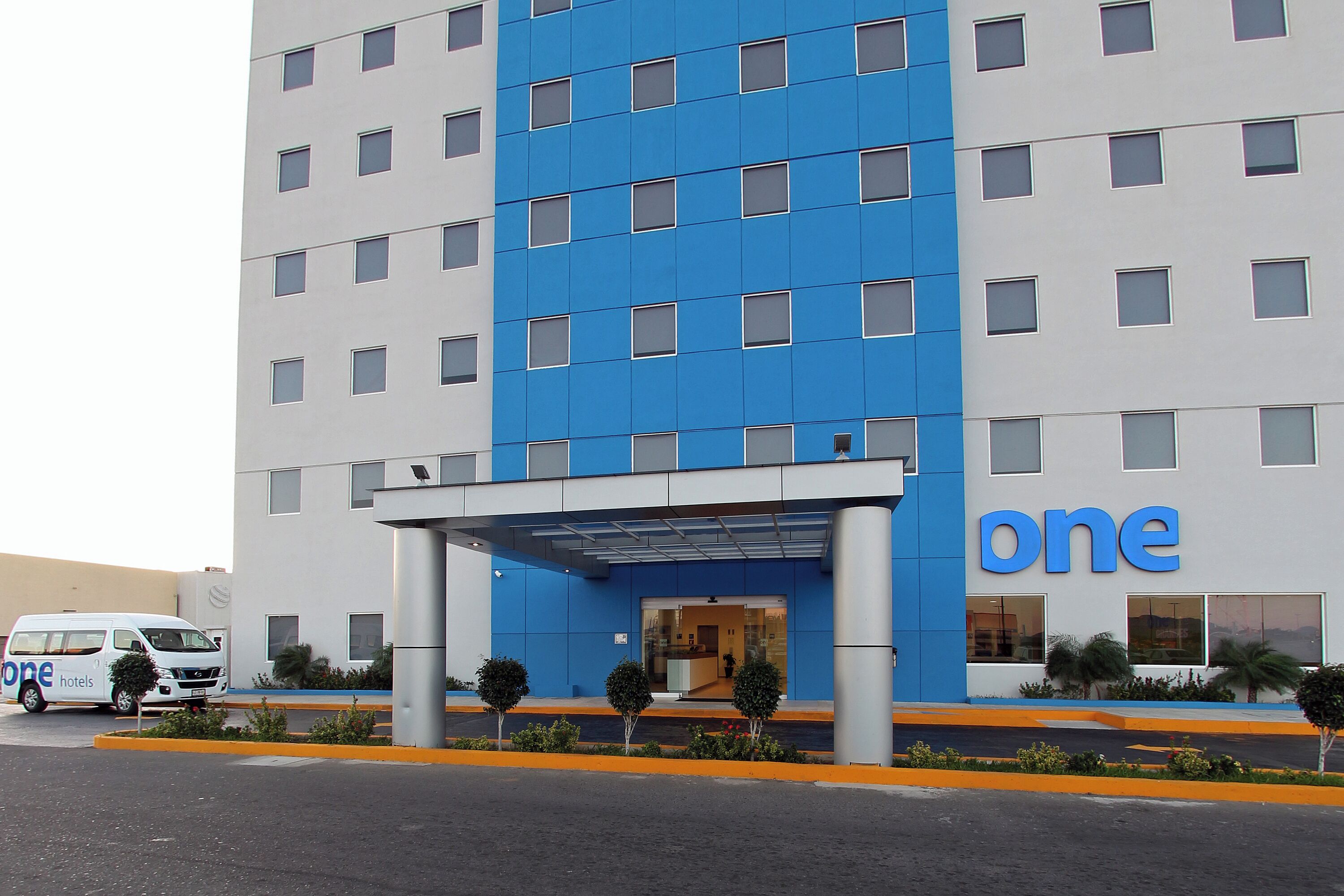 Un hotel moderno con fachada azul y blanca, un acceso cubierto y una furgoneta estacionada afuera.