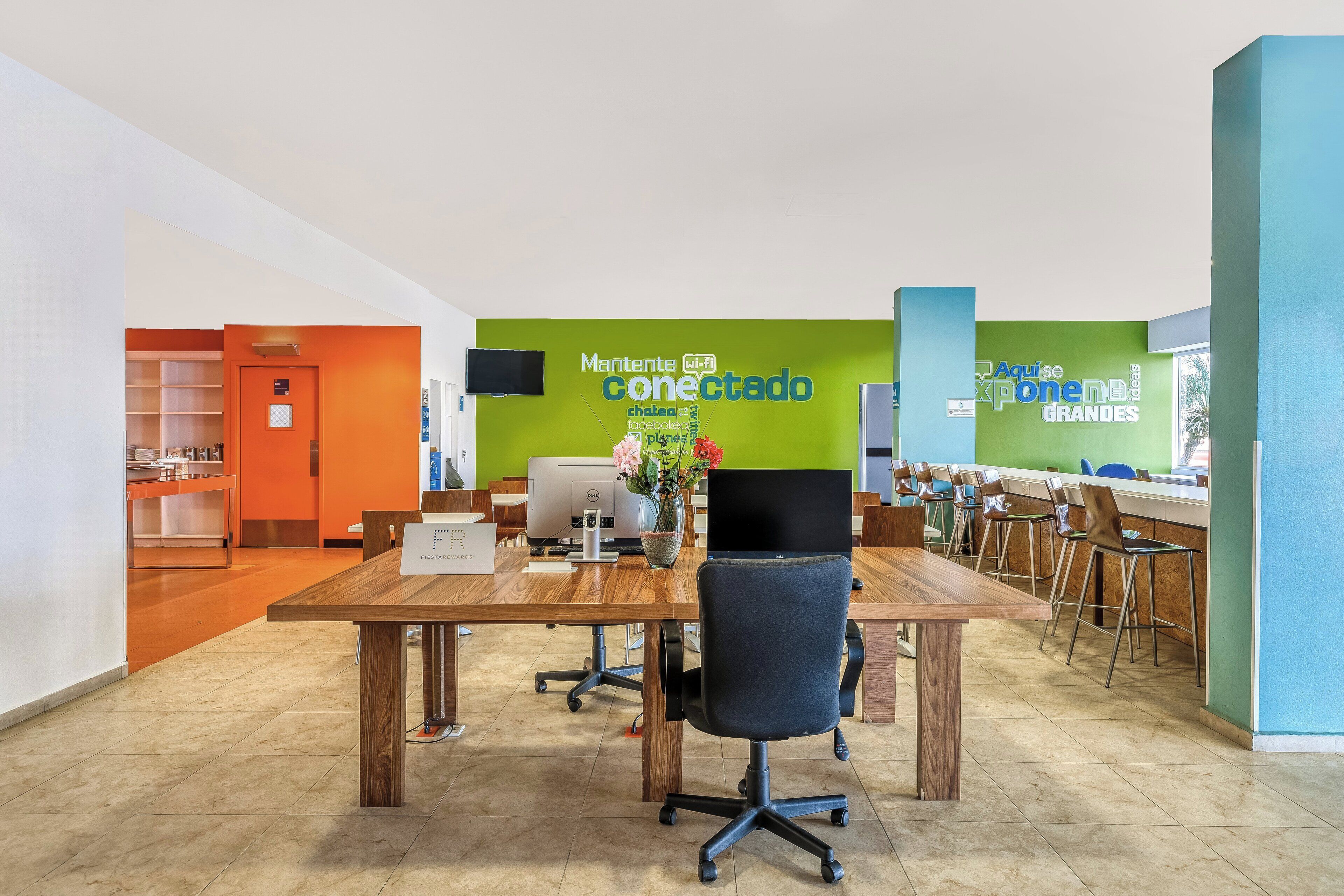 A modern office space with a wooden table, office chairs, and a green wall with text.