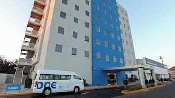 Un moderno edificio de hotel con fachada blanca y azul, una entrada cubierta y una furgoneta estacionada adelante.