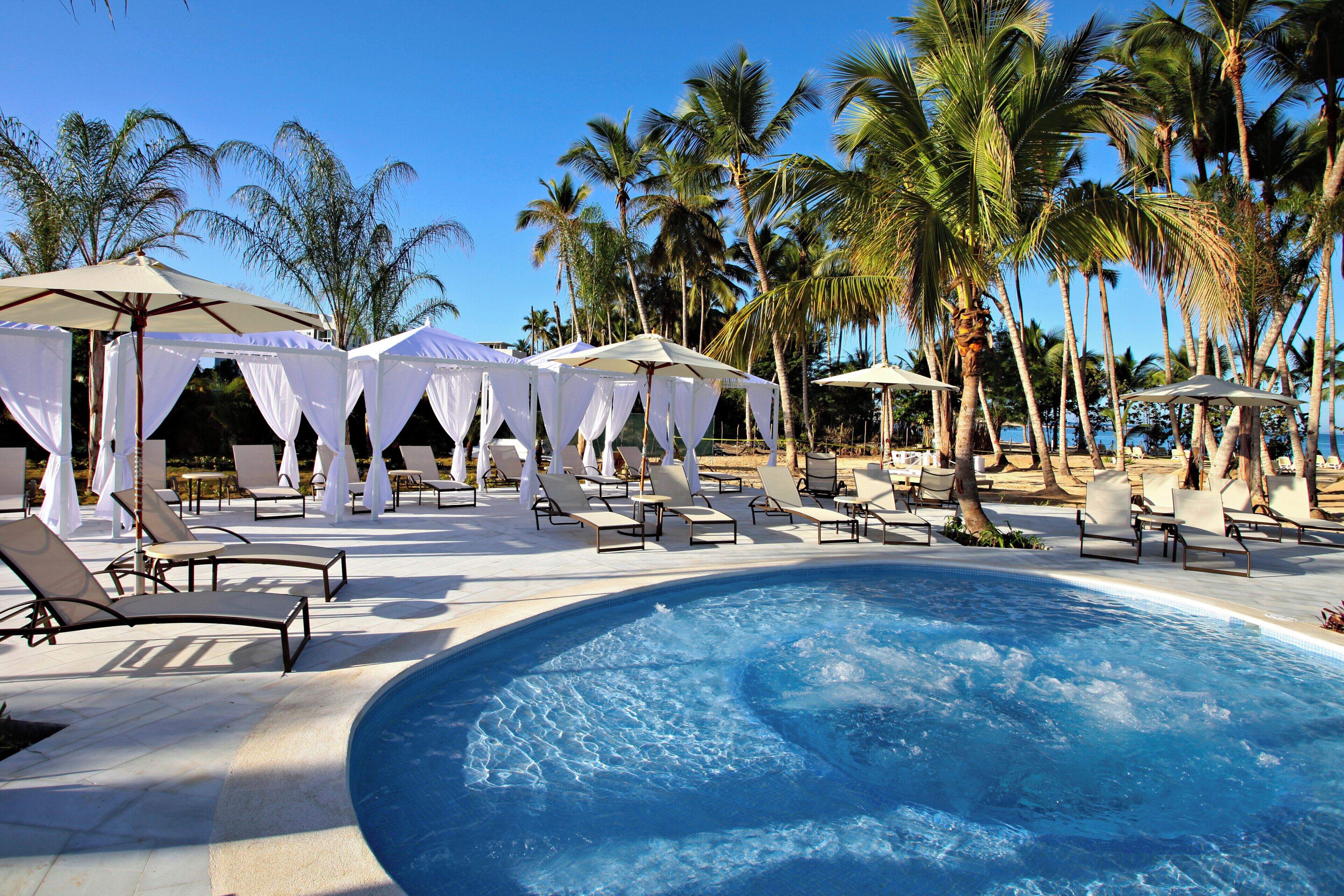 A pool area with lounge chairs and umbrellas, surrounded by palm trees.