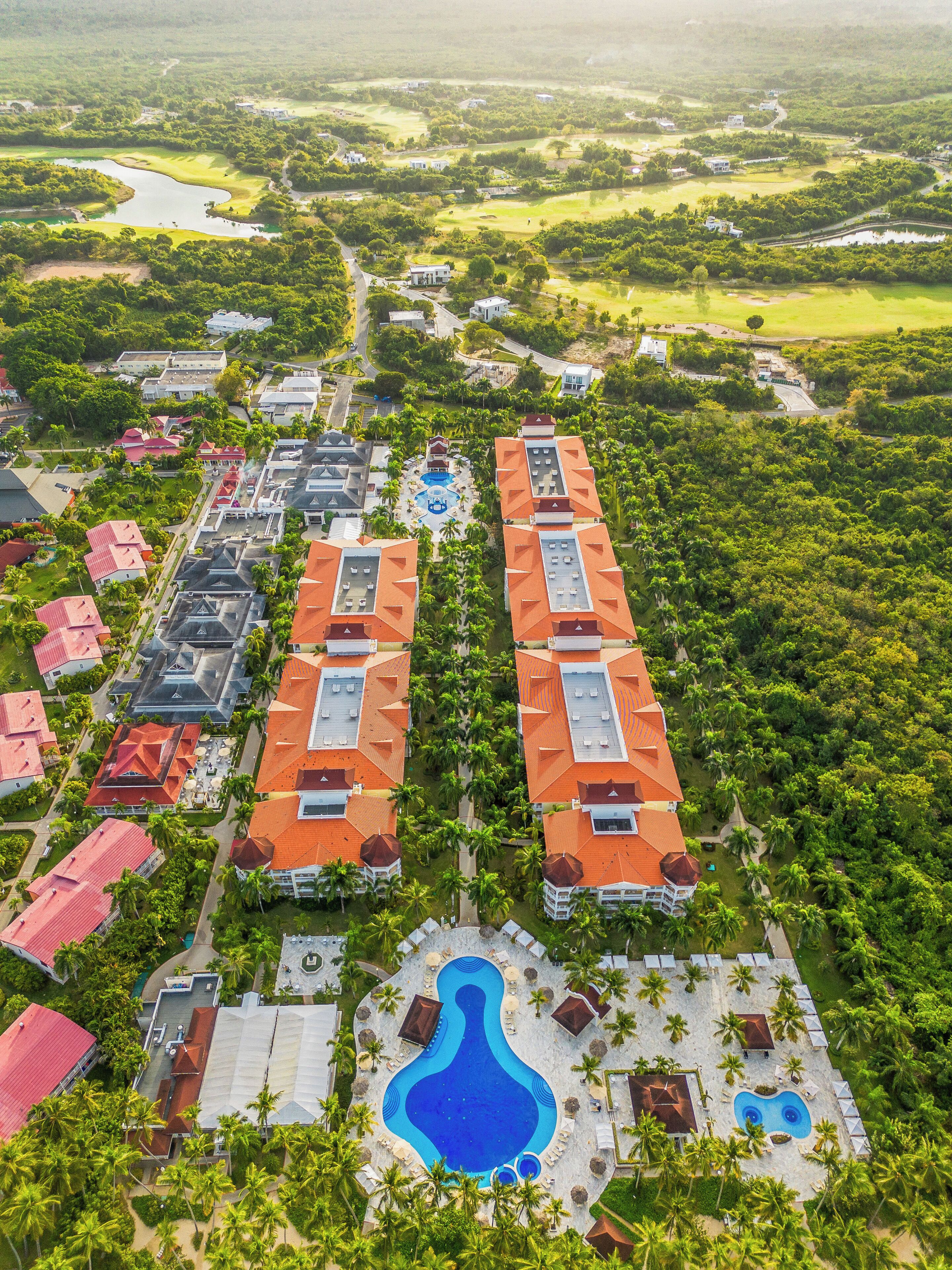 An aerial view of a resort with multiple buildings, a central swimming pool, and surrounding greenery.