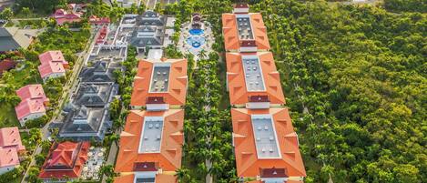An aerial view of a resort with multiple buildings, a central swimming pool, and surrounding greenery.