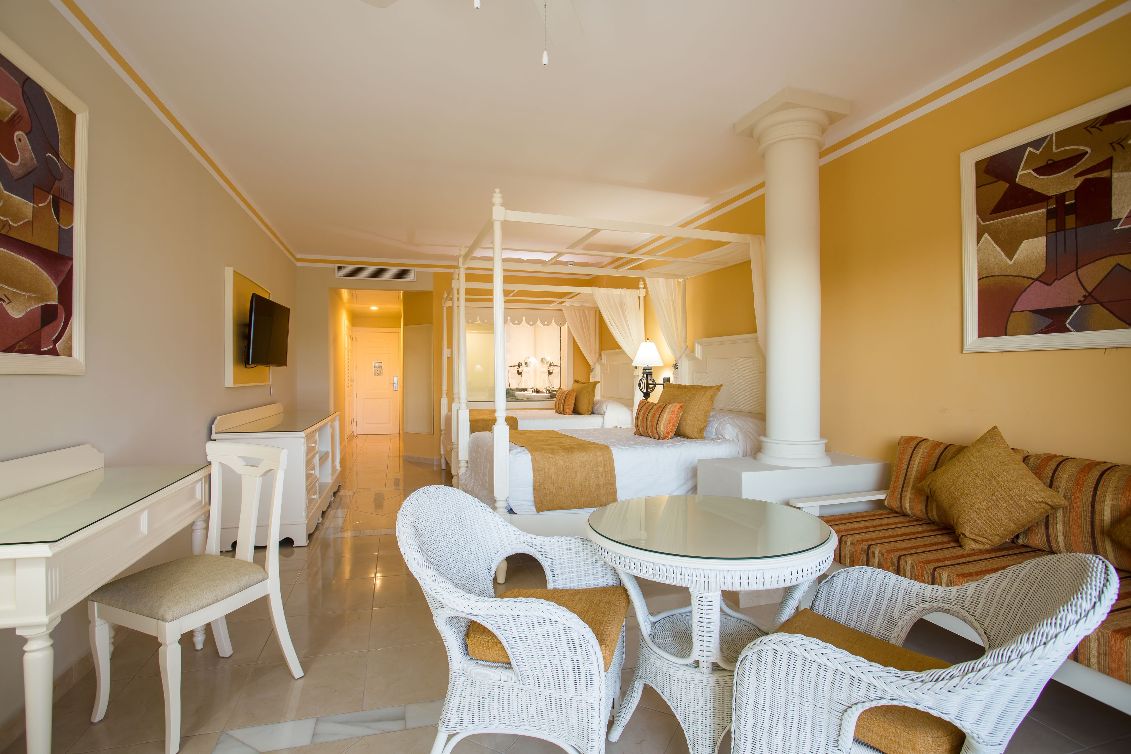 Une chambre d’hôtel dotée d’un lit à baldaquin, d’un coin salon avec des meubles en osier, d’une table à manger et d’un téléviseur.