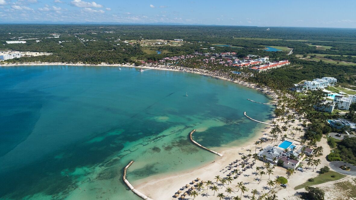 Vista aérea de un complejo turístico frente al mar, con playa, aguas cristalinas y una combinación de edificios del resort.