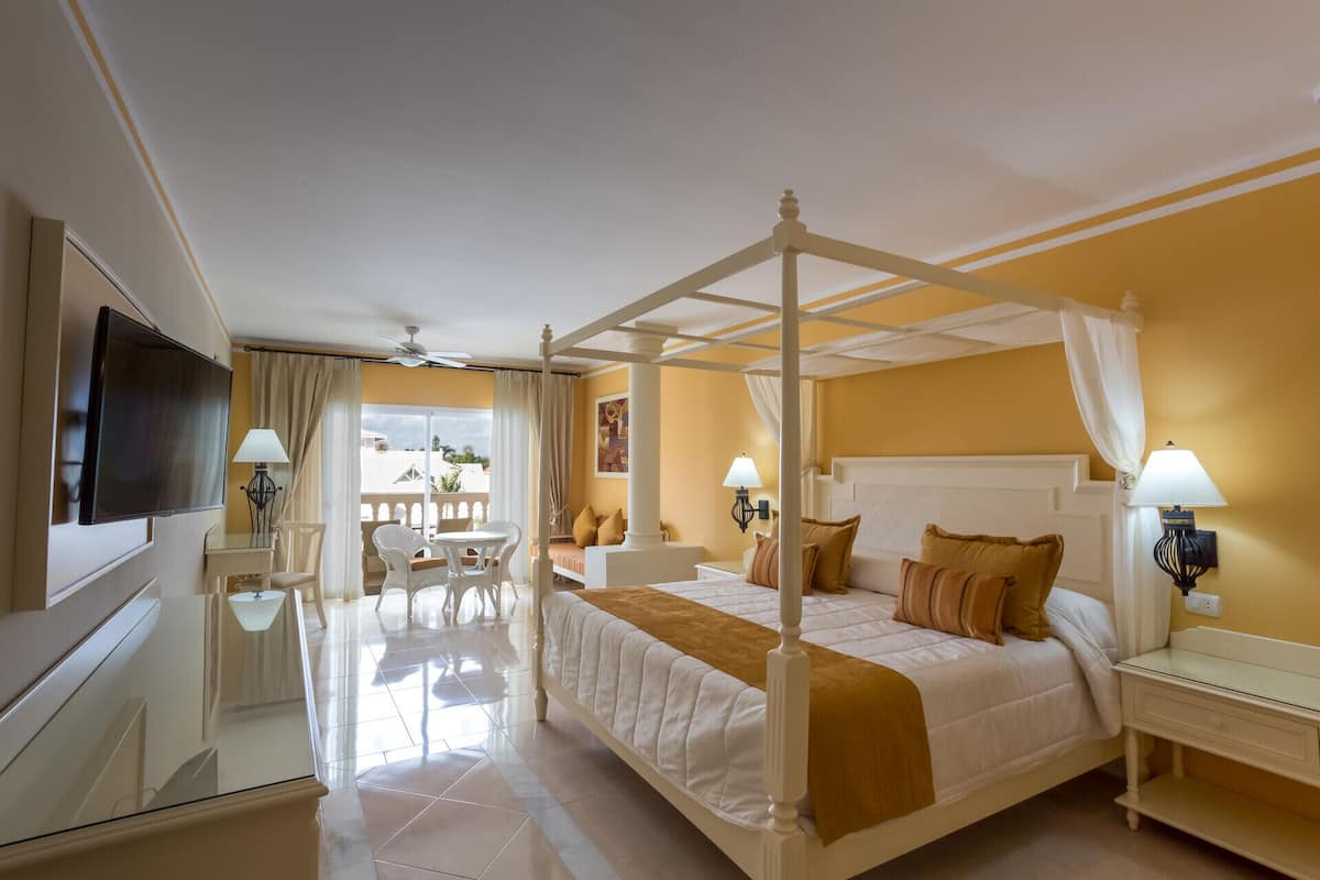 Una cama con dosel y mosquitera, un televisor montado en la pared y un balcón con mesa y sillas.