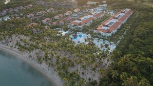 Vista aérea de un resort con varias edificaciones, una playa y una zona de piscina.