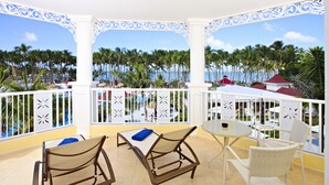 A balcony with white wicker furniture, a small round table, and a view of palm trees and the ocean.