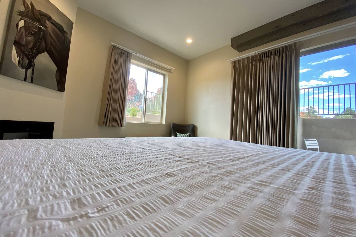 Ein Hotelzimmer mit einem großen Bett, einem Fenster mit Vorhängen, einem Sessel und einem Gemälde eines Pferdes an der Wand.