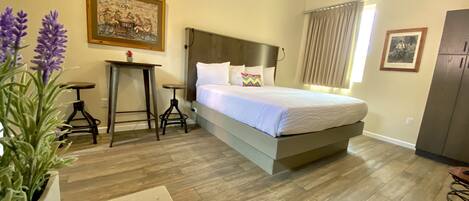 A bedroom with a large bed, two small tables, a potted plant, and a painting on the wall.