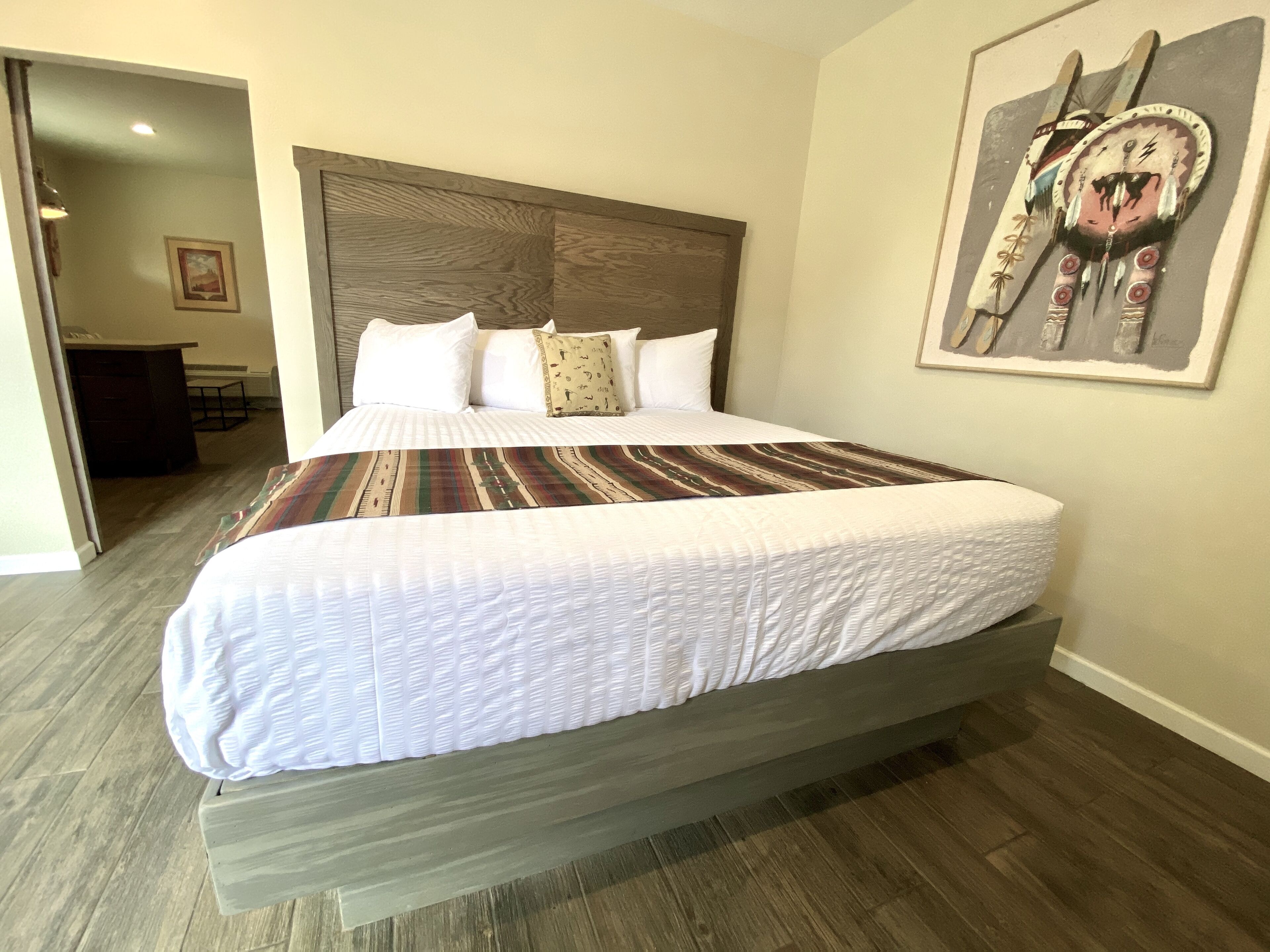 Een groot bed met een houten hoofdbord, een gebreid plaid en witte lakens.