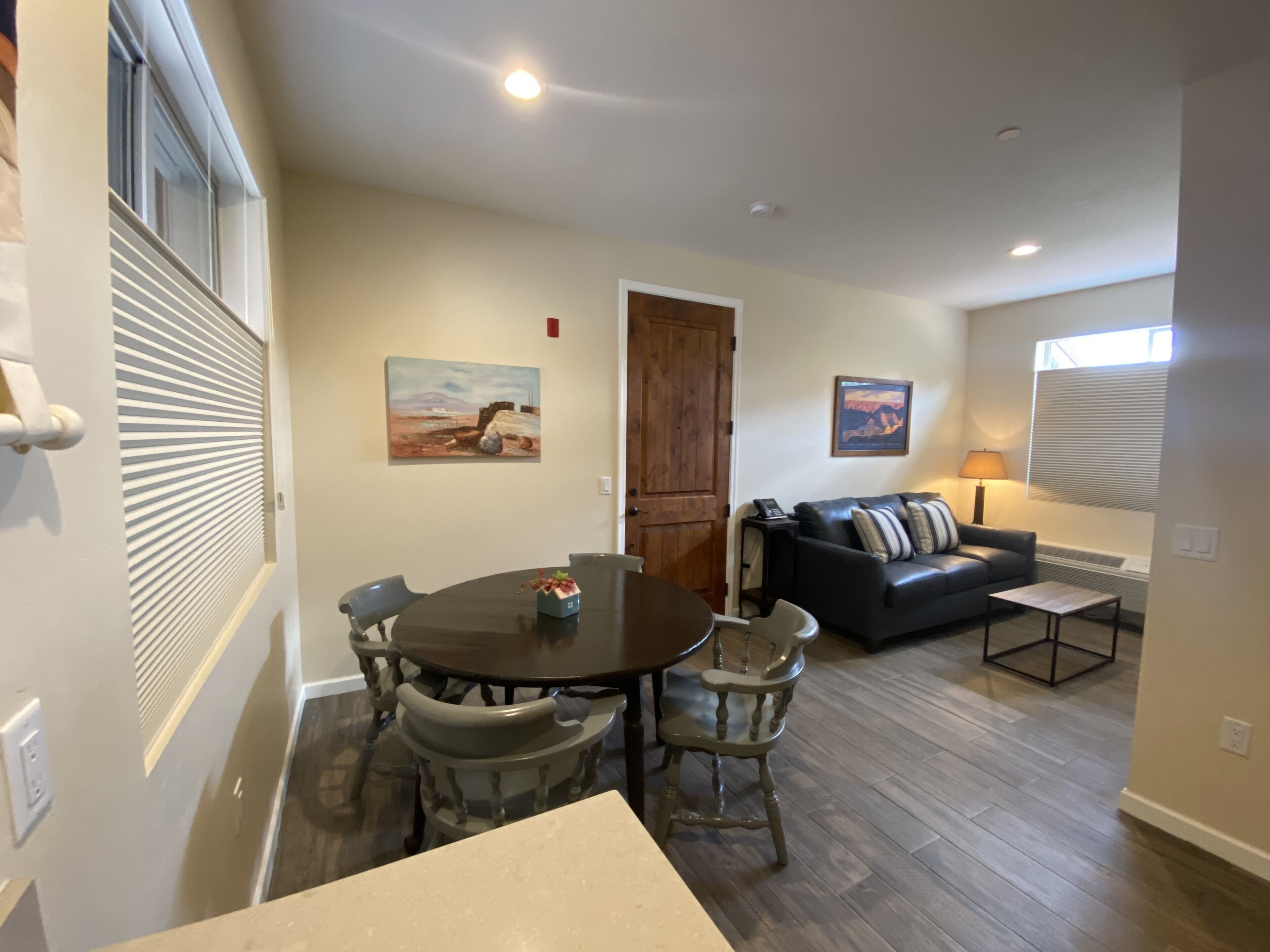 A dining area with a round table and chairs, a living room with a sofa and a lamp, and two paintings on the walls.