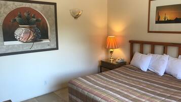 Une chambre d’hôtel avec un lit, une table de chevet avec une lampe, un téléphone et deux tableaux encadrés au mur.