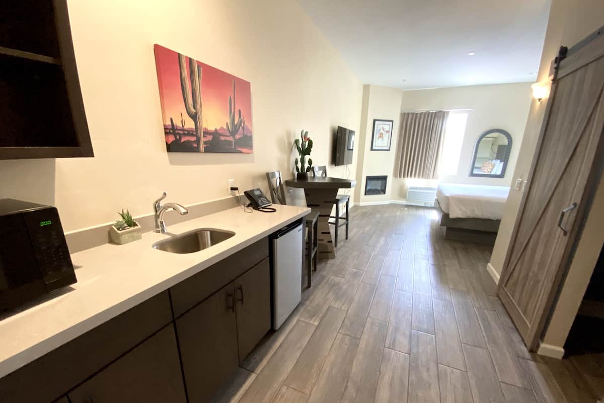 Eine moderne Küche mit integriertem Mikrowellenherd, Spüle und Arbeitsplatte. Es gibt einen Essbereich mit Tisch und Stühlen, sowie ein Schlafzimmer mit Bett und Fenster.