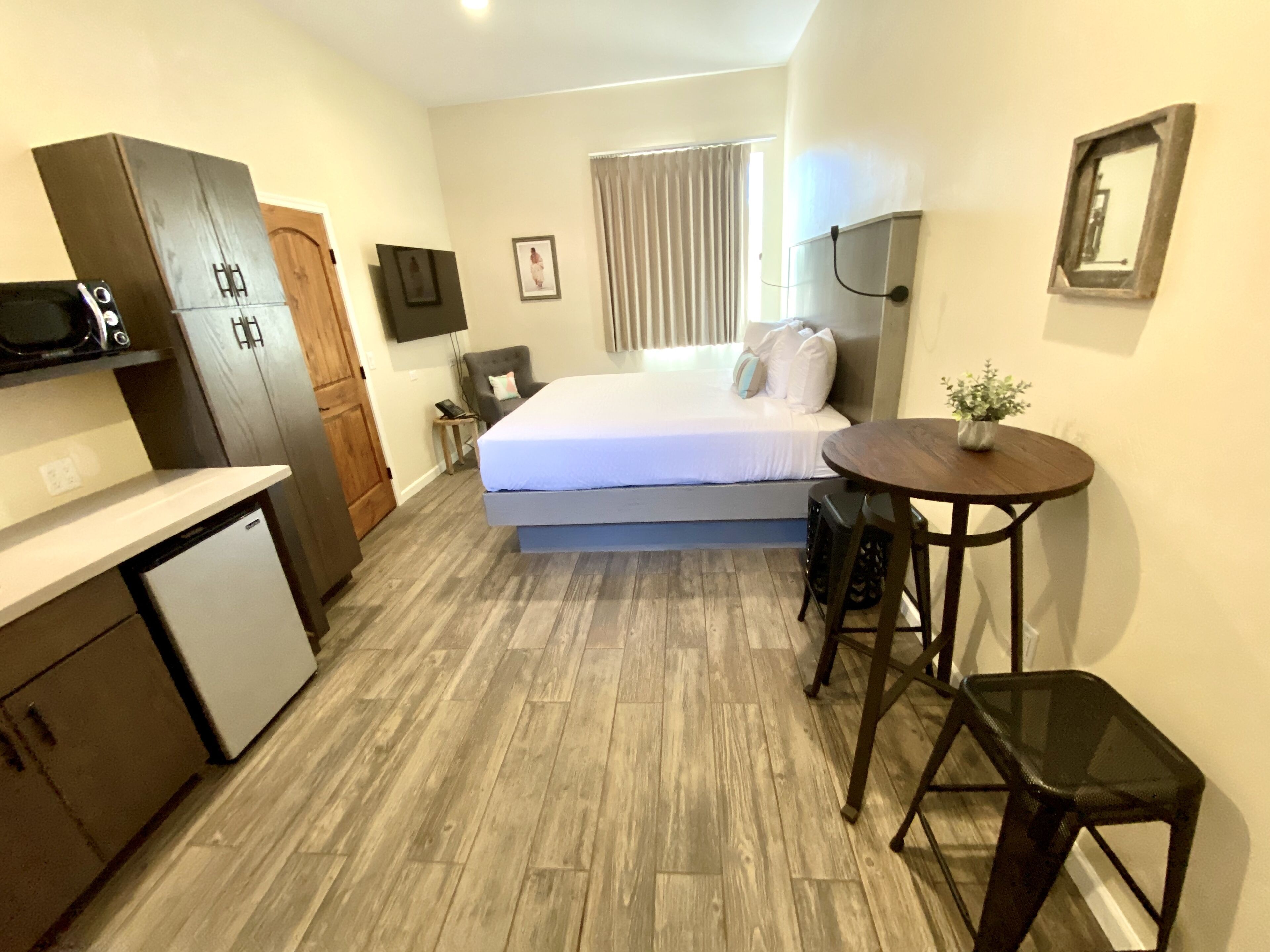 Una habitación de hotel compacta con cama, una kitchenette pequeña, una mesa de comedor y una sola silla.