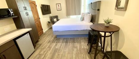 Una habitación de hotel compacta con cama, una kitchenette pequeña, una mesa de comedor y una sola silla.