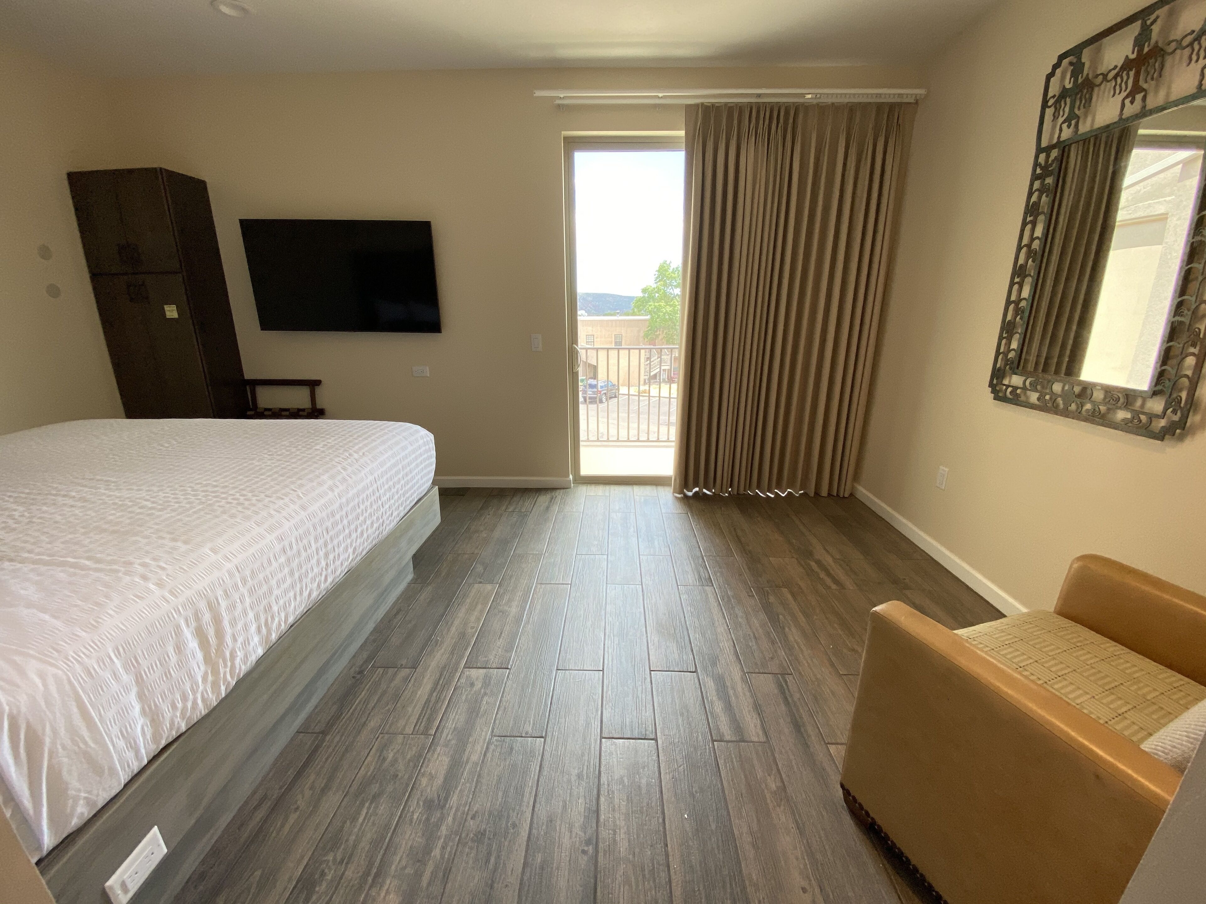 A hotel room with a large bed, a chair, a television, and a balcony with curtains.