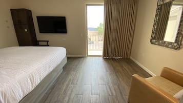 A hotel room with a large bed, a chair, a television, and a balcony with curtains.