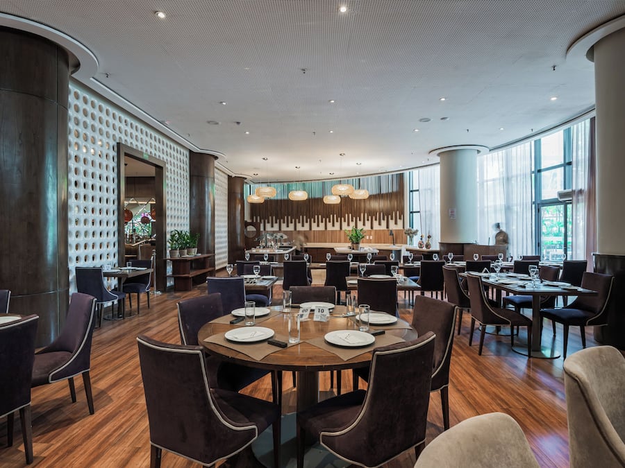 A spacious restaurant with multiple dining areas, large windows, and a modern ceiling design.