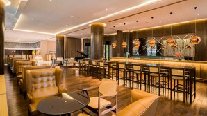 Een ruime lobby met lederen zitplaatsen, een piano en een bar met een decoratieve wand.