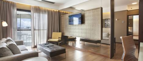 Una habitación de hotel moderna con un sofá grande, una mesita, una silla y un televisor montado en la pared.