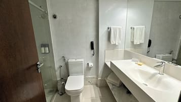 Uma casa de banho moderna com sanita, bidé e um espelho grande sobre uma sanefa branca.