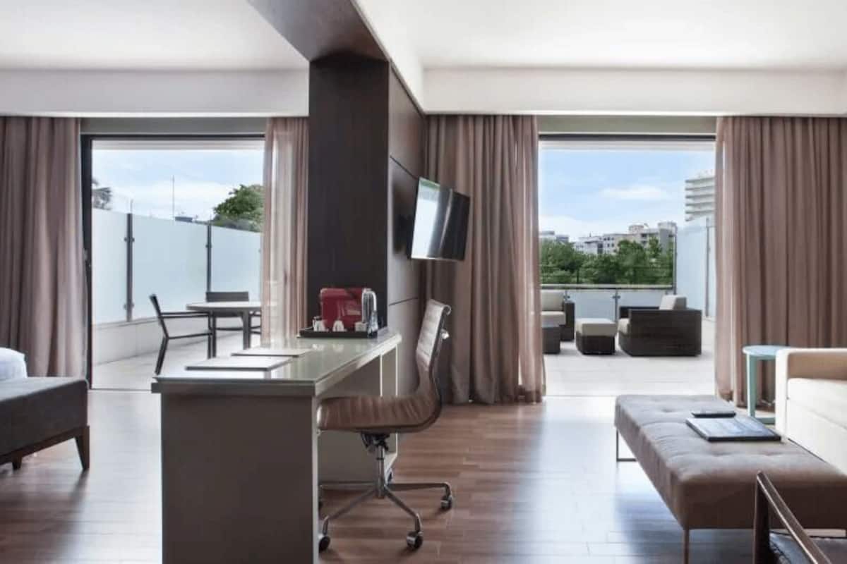 Une chambre d’hôtel moderne équipée d’un bureau, d’un canapé et d’un balcon avec coin salon extérieur.