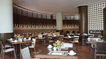 A spacious dining area with multiple tables and chairs, a high ceiling with recessed lighting, and a decorative wall with vertical slats.