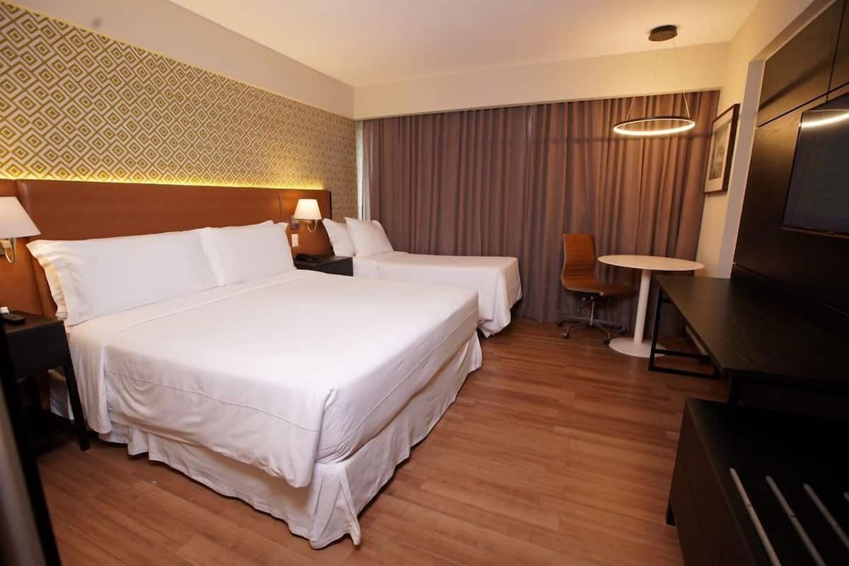 Une chambre d’hôtel avec un grand lit, deux tables de chevet, un bureau, une chaise, une télévision et un mur décoré d’un motif.