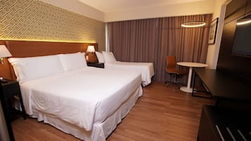 A hotel room with a large bed, two bedside tables, a desk, a chair, a TV, and a patterned wall.