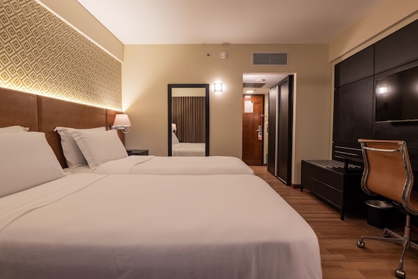 A hotel room with two beds, a desk, a chair, and a TV.