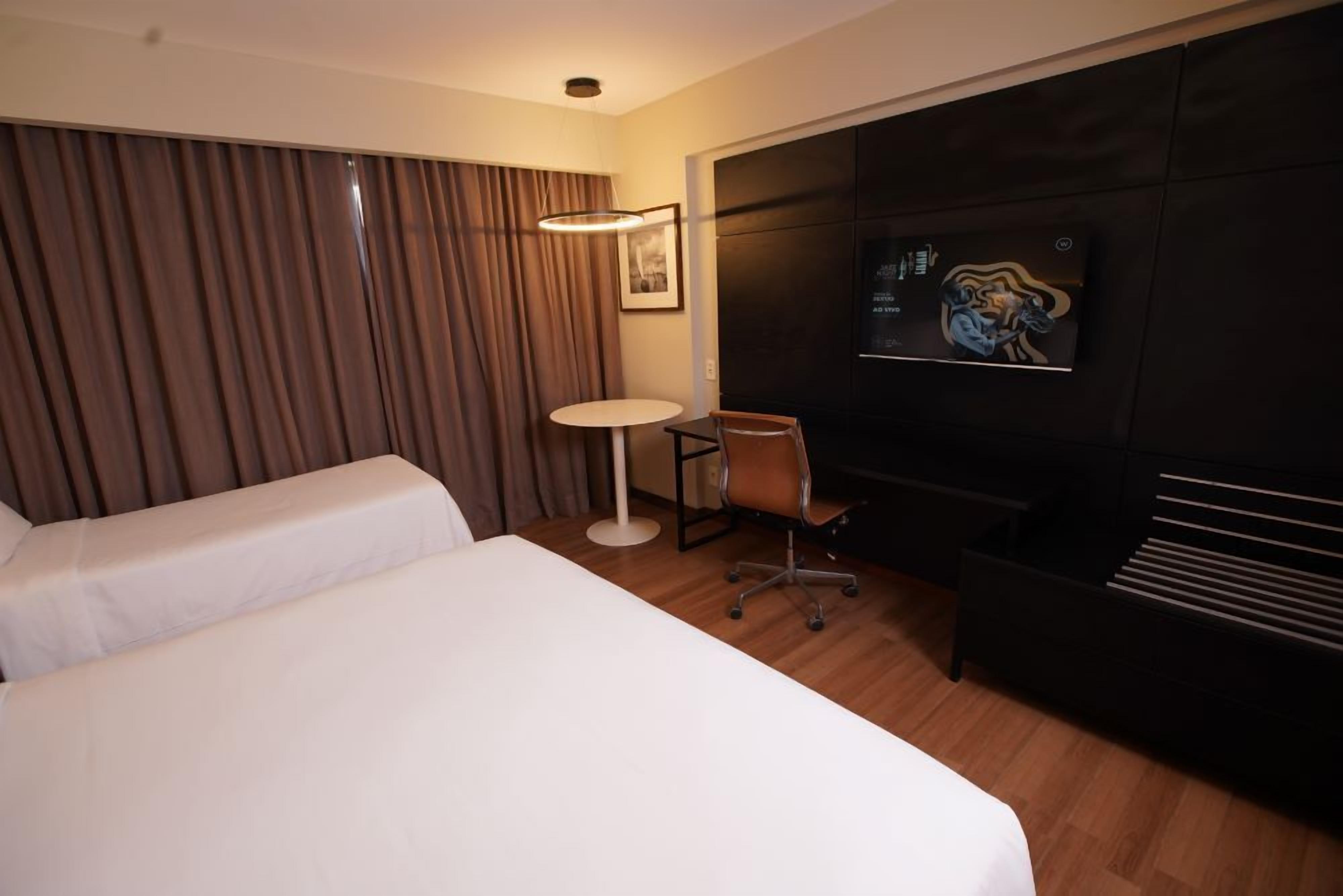 Habitación de hotel con dos camas, un escritorio, una silla, un televisor y un televisor montado en la pared.