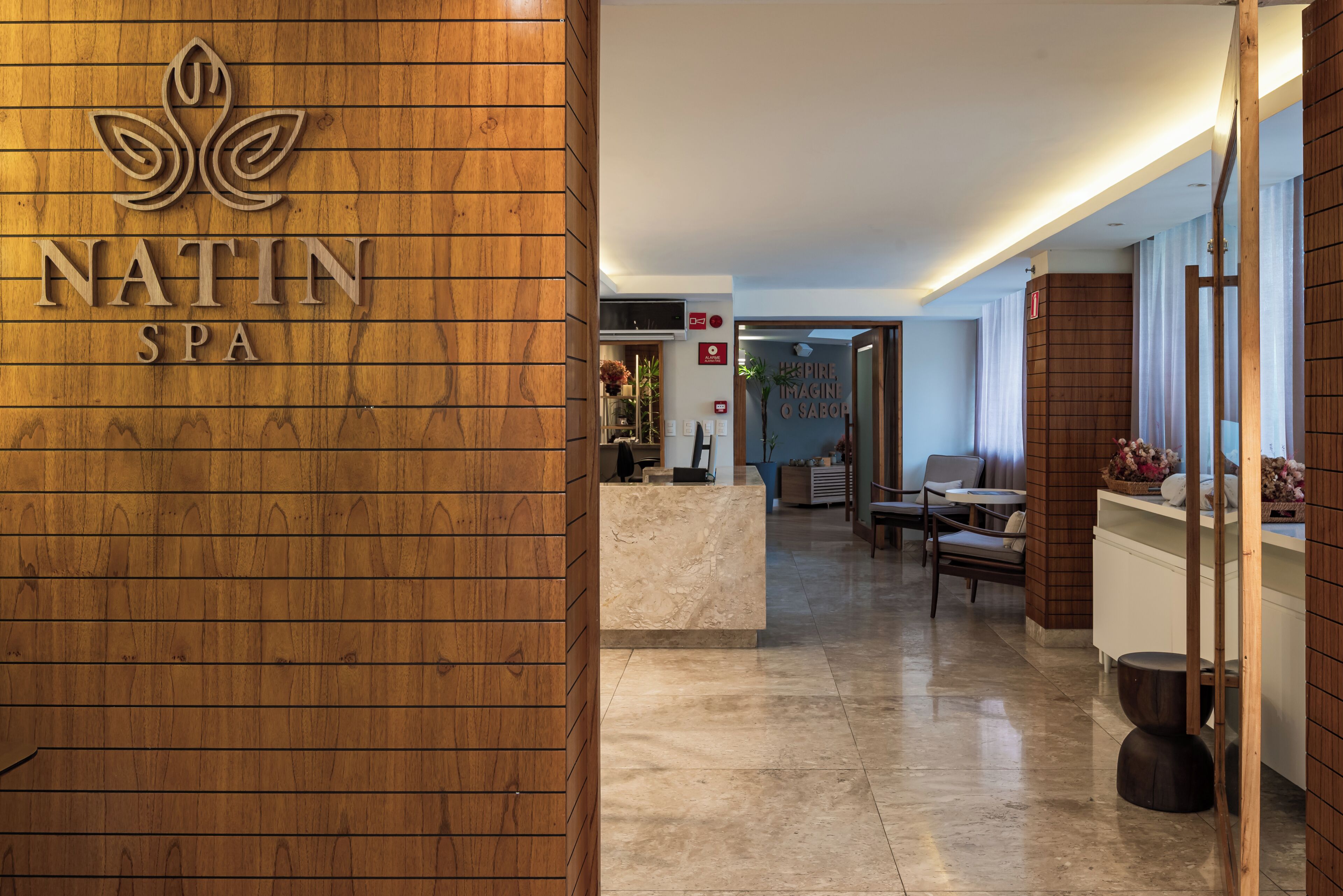 Un área de recepción con una pared de madera, un mostrador de recepción y un letrero que dice 'NATIN SPA'.