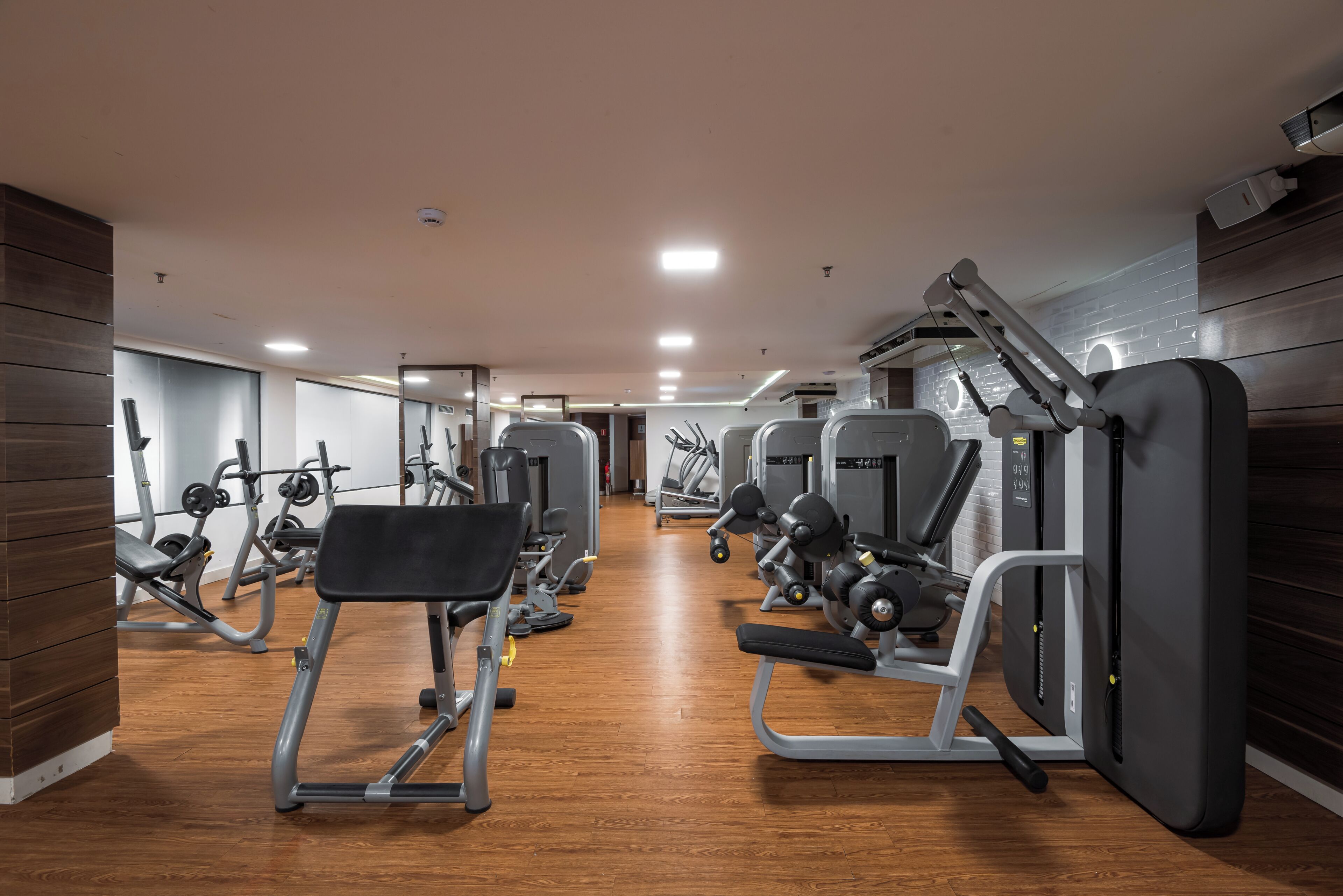 Une salle de sport équipée de divers appareils d’exercice, dotée d’un plancher en bois et d’un mur recouvert de miroirs.