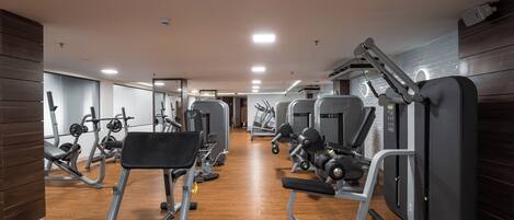 Une salle de sport équipée de divers appareils d’exercice, dotée d’un plancher en bois et d’un mur recouvert de miroirs.