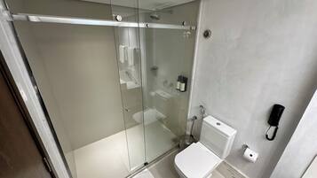 A modern bathroom with a glass-enclosed shower, a toilet, and a hand dryer.