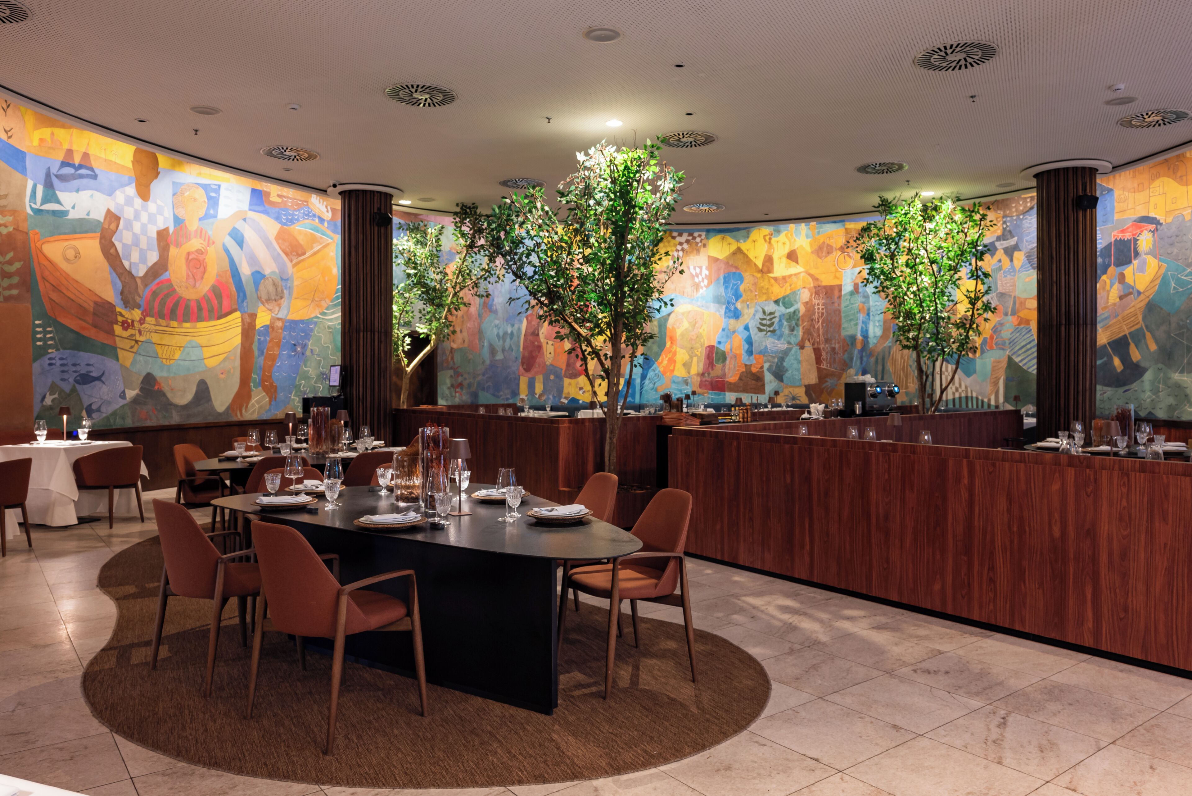 A restaurant with a large mural, wooden bar, and round tables with chairs.