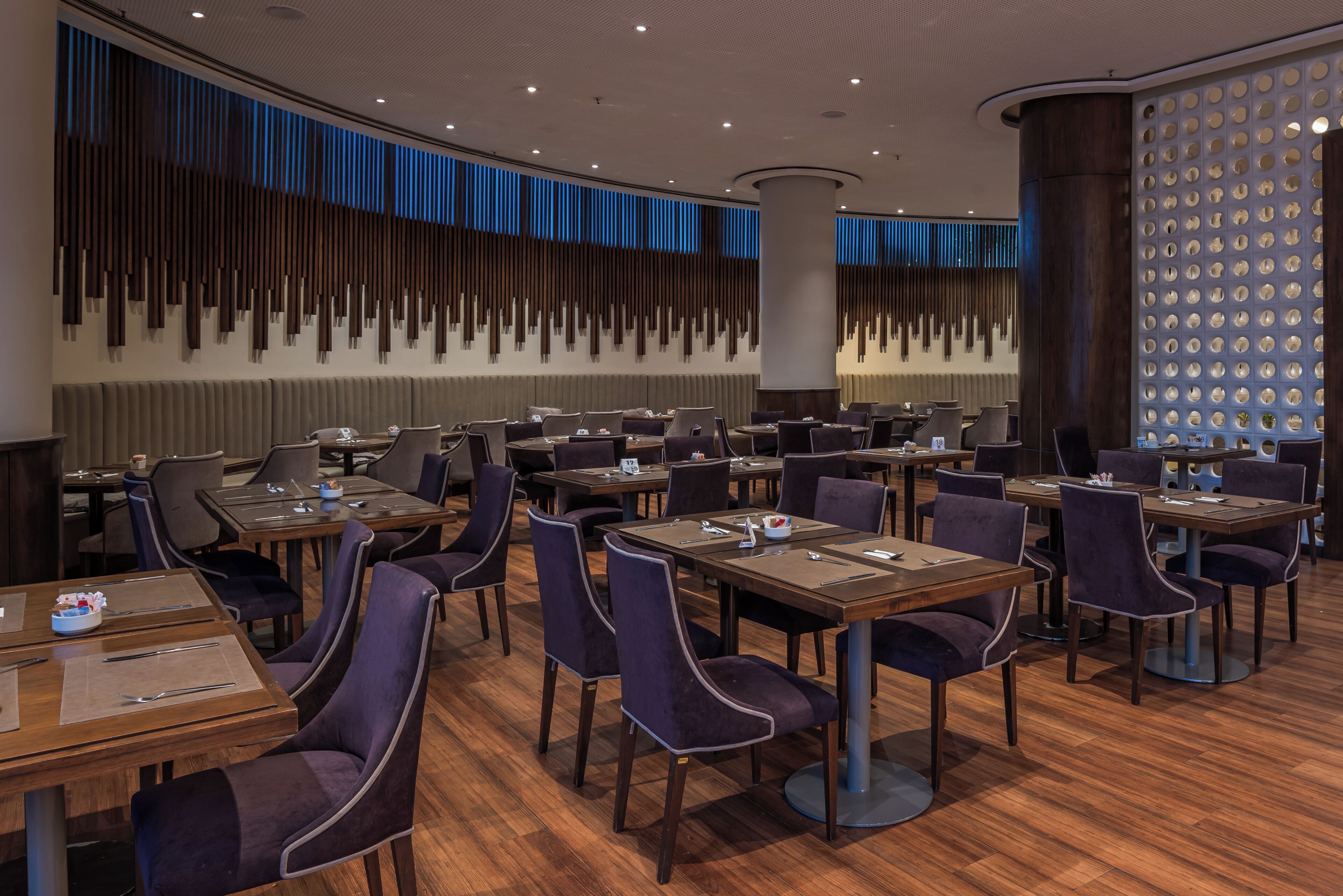 Un espace de restauration moderne, doté de plusieurs tables et chaises, d’un mur décoratif agrémenté d’éléments verticaux et d’une colonne circulaire.
