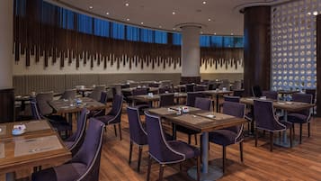 Un espace de restauration moderne, doté de plusieurs tables et chaises, d’un mur décoratif agrémenté d’éléments verticaux et d’une colonne circulaire.