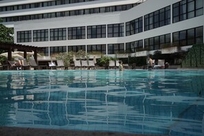 A swimming pool with lounge chairs and a building with large windows in the background.