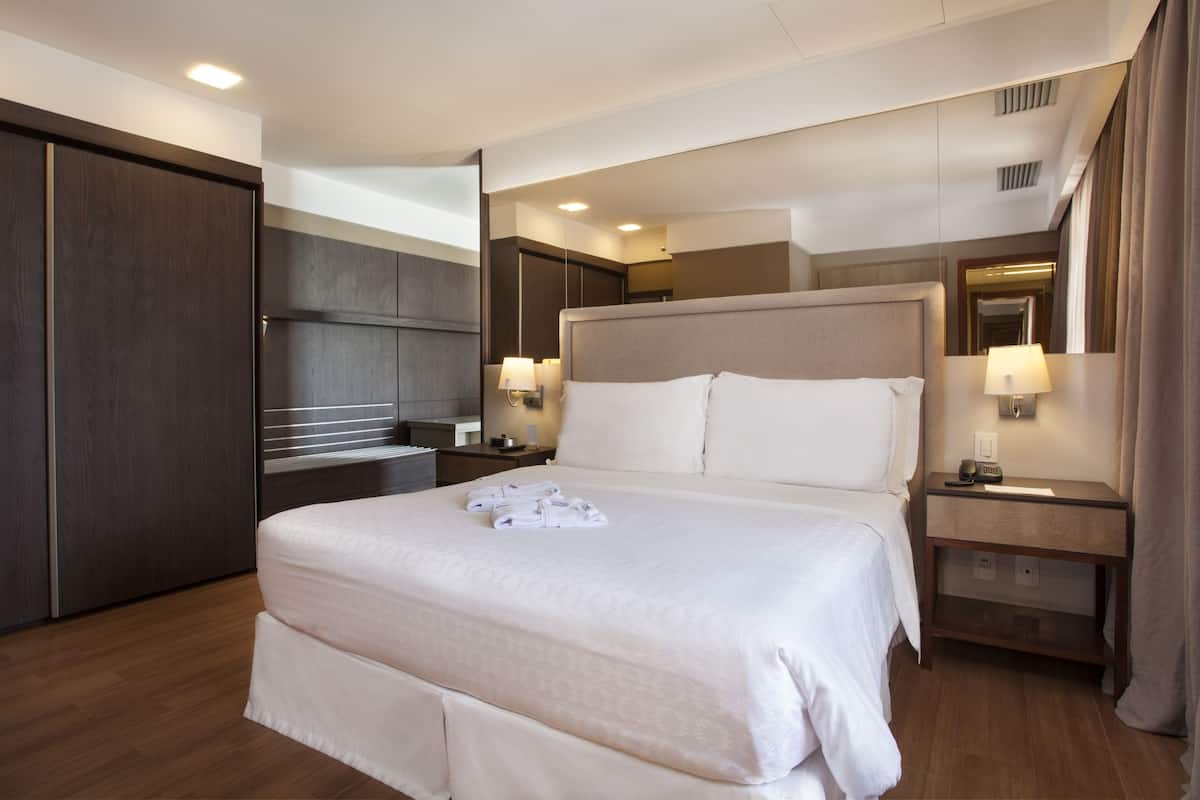 Une chambre d’hôtel moderne avec un grand lit, des tables de chevet, une armoire et un miroir.