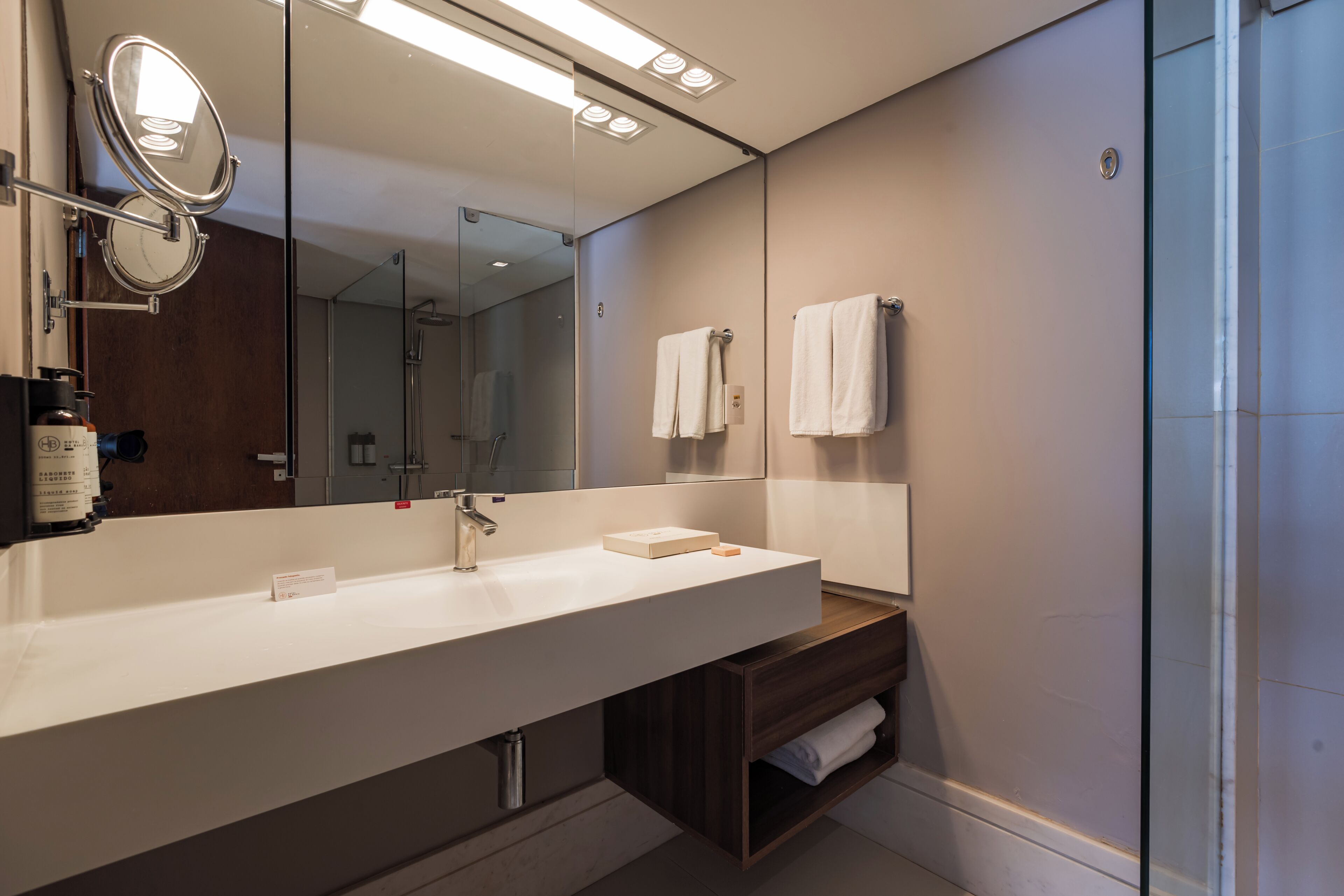 A modern bathroom with a large mirror, a white sink, and a glass shower enclosure.